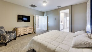 Een slaapkamer met een groot bed, een dressoir, een televisie aan de muur en een deur naar een andere kamer.
