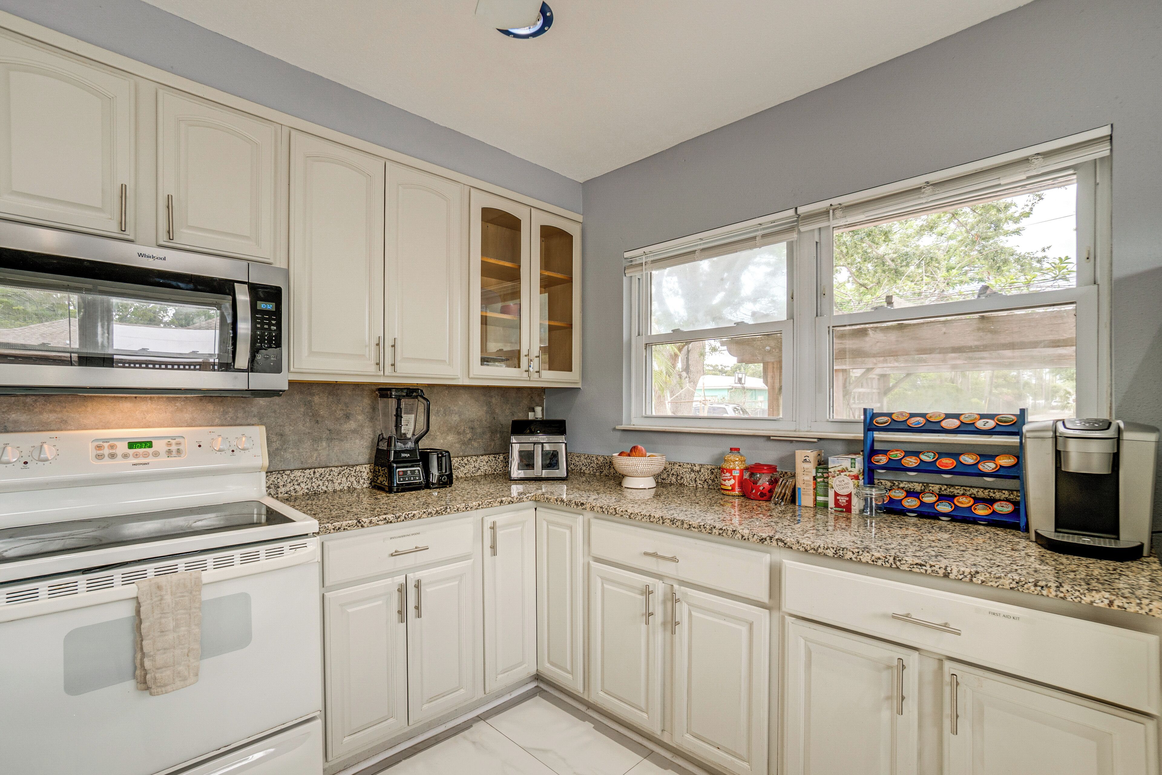 A kitchen with white cabinets, a microwave, a stove, a coffee maker, and a window with a view of trees.