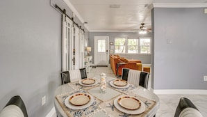 Un comedor con una mesa dispuesta para cuatro, una puerta corredera y vistas a una sala de estar con sofá y sillones.