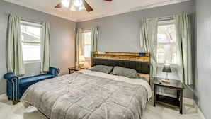 Un dormitorio con cama, mesita de noche, lámpara, silla y ventilador de techo.