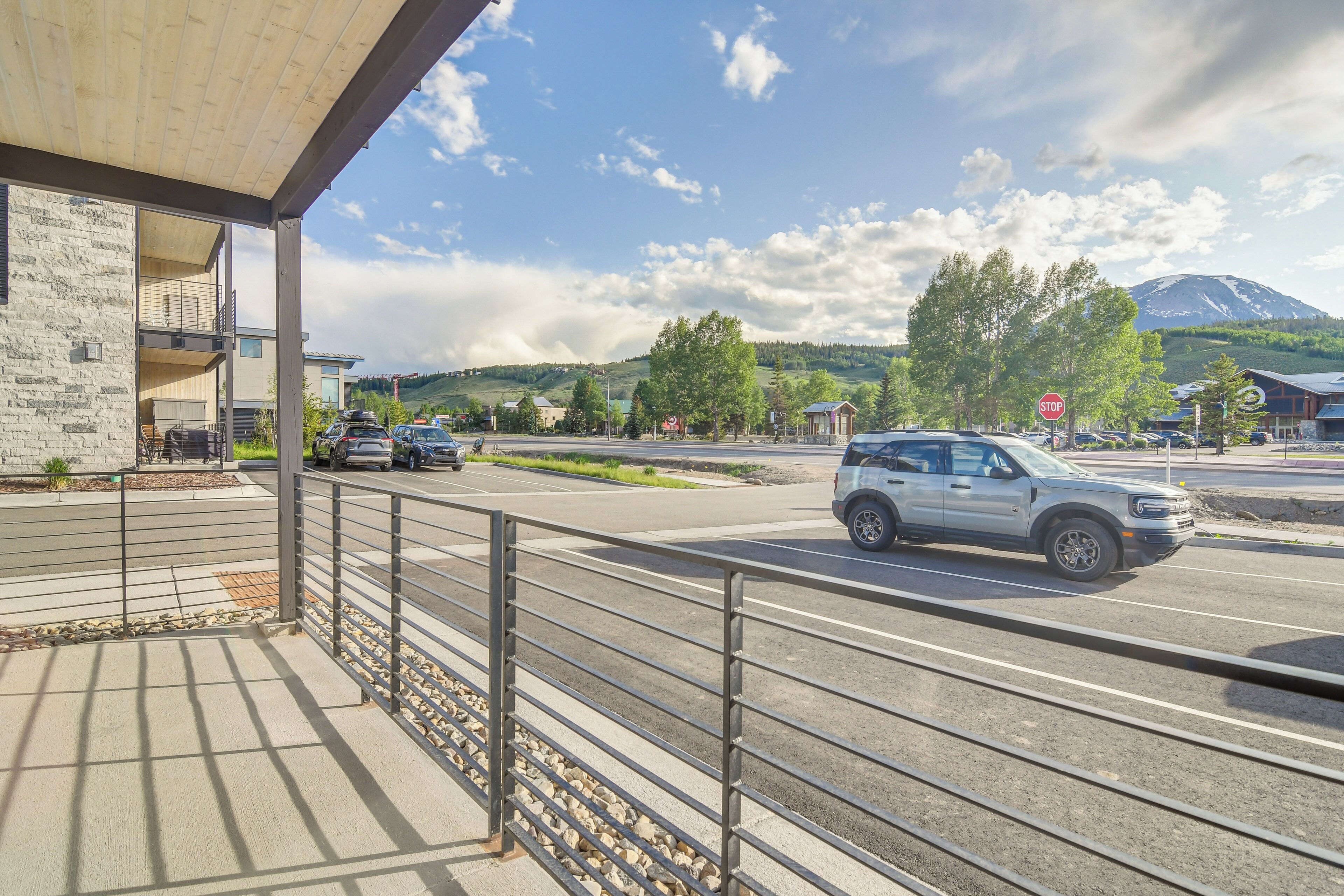 A modern building with a covered outdoor area, a road with cars, and a mountain in the background.