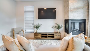 A living room with a fireplace, a mounted TV, and a seating area with cushions. - 3 Mi to Lake Dillon: Condo Near Shops & Eats! (Silverthorne)