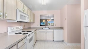 Een keuken met witte apparaten, lichtroze wanden en een raam met uitzicht.