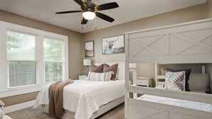 A bedroom with a bed, a ceiling fan, a window with blinds, and artwork on the wall. - Hot Tub + Outdoor Kitchen: Stylish Home in Bryan (Bryan)