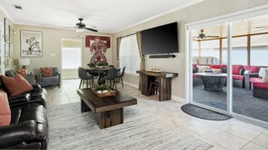 A living room with a sofa, coffee table, TV, and a dining area with chairs and a table. - Hot Tub + Outdoor Kitchen: Stylish Home in Bryan (Bryan)