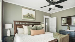 A bedroom with a bed, a nightstand, a dresser, a ceiling fan, and a painting on the wall. - Hot Tub + Outdoor Kitchen: Stylish Home in Bryan (Bryan)