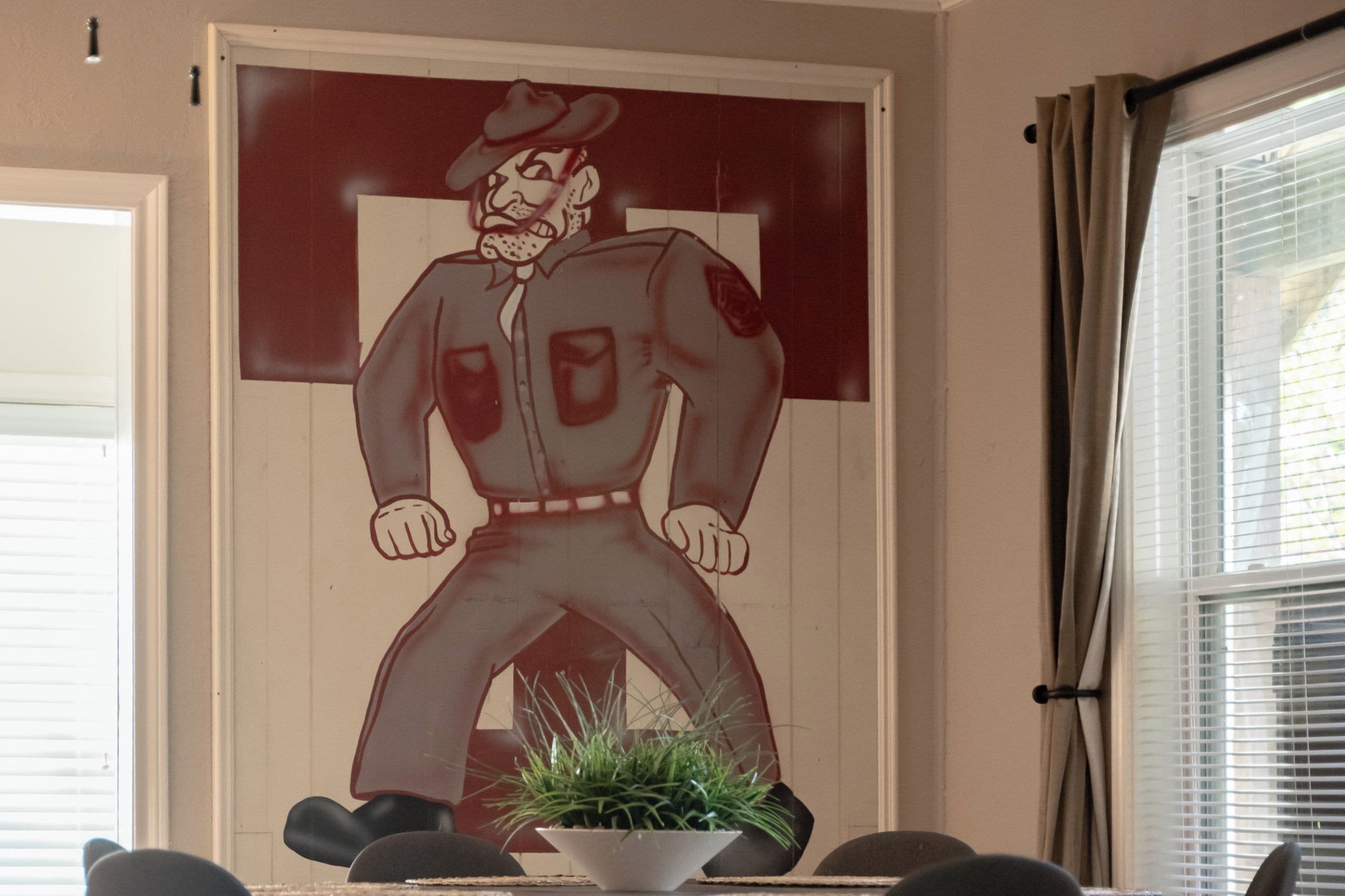 Een vergaderruimte met een groot poster van een stripfiguur, een plant in pot op tafel en een raam met jaloezieën.