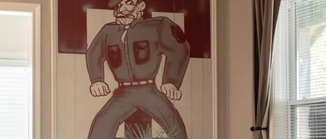 Un salón de conferencias con un cartel grande de un personaje de caricatura, una planta en maceta sobre la mesa y una ventana con persianas.