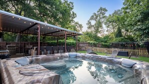 A hot tub with seating, a covered patio area, and a wooden fence. - Hot Tub + Outdoor Kitchen: Stylish Home in Bryan (Bryan)