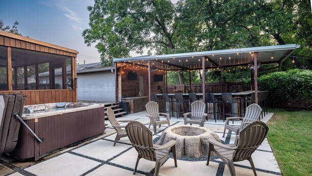 An outdoor patio with a hot tub, seating area, and a covered barbecue area. - Hot Tub + Outdoor Kitchen: Stylish Home in Bryan (Bryan)