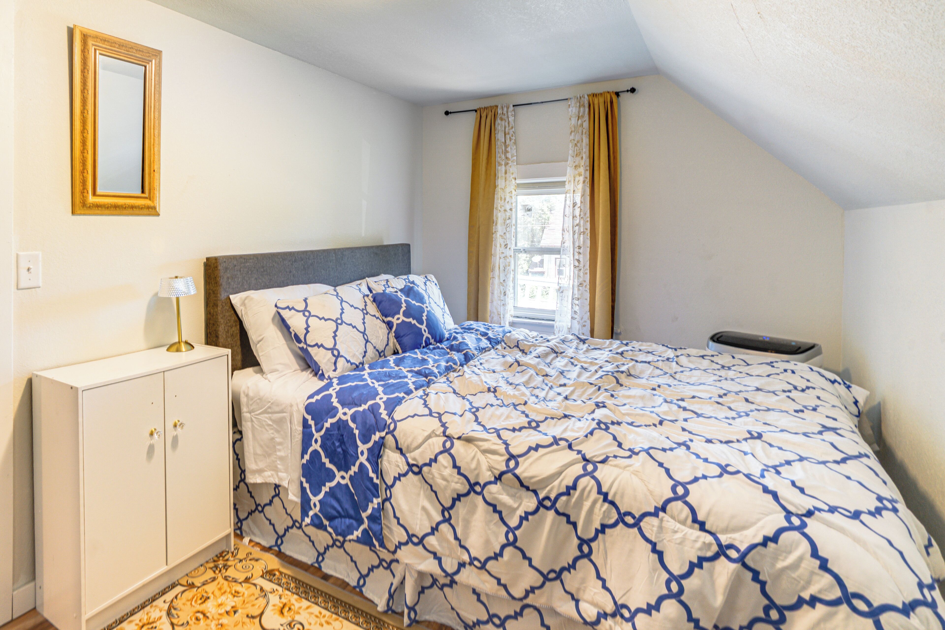 A bedroom with a bed, a nightstand, a lamp, a wardrobe, and a window with curtains.