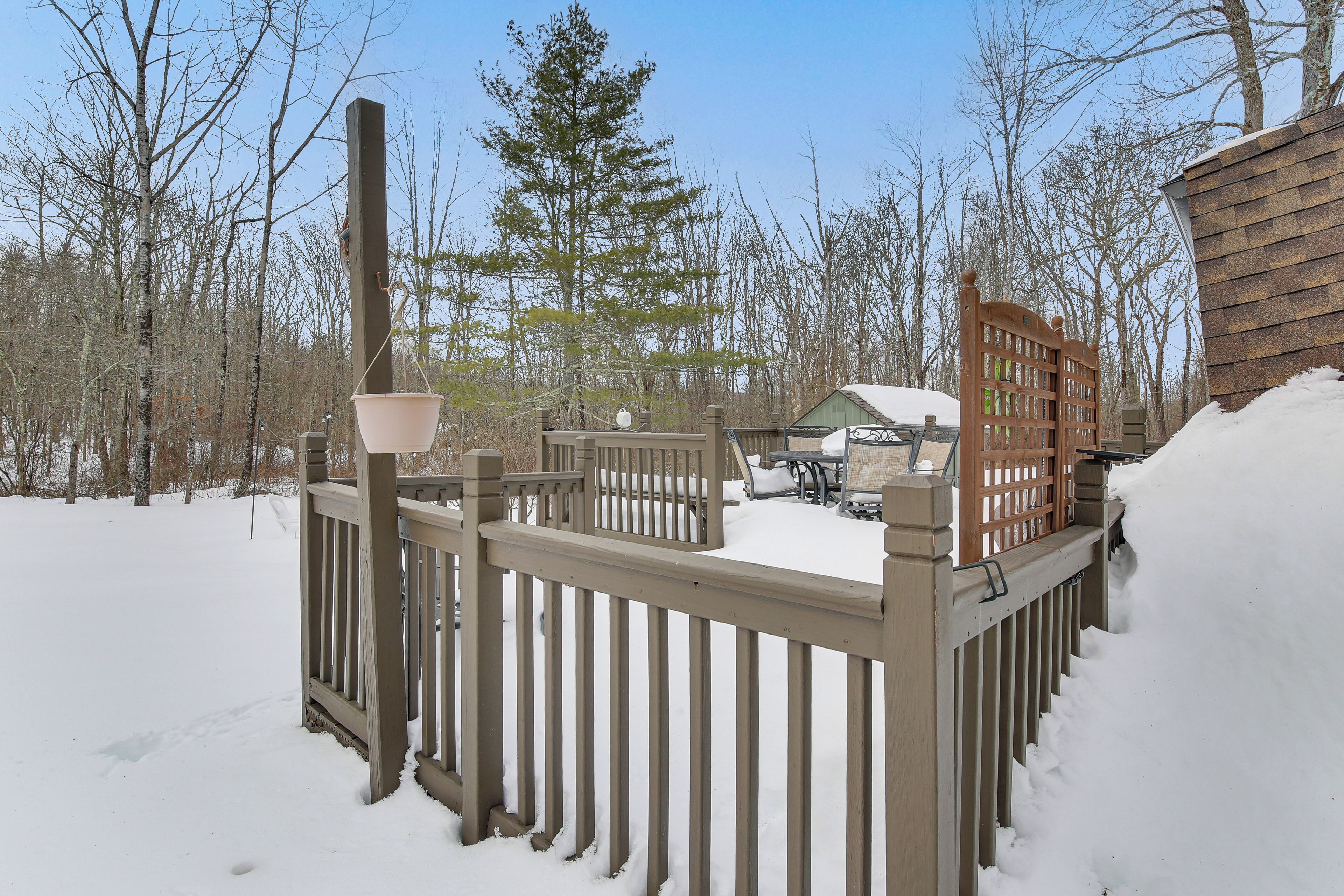 A wooden deck with a snow-covered ground, a metal railing, and a wooden fence.