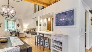 Un vaste espace de vie doté d’un plancher en bois, d’une table à manger avec des chaises, d’un coin cuisine avec un comptoir blanc et d’un grand plan architectural encadré accroché au mur.