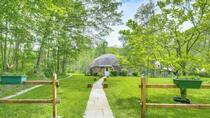 Un chemin menant à une maison entourée d’une v égétation luxuriante et d’arbres.