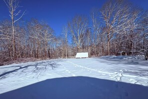 Un paysage enneigé avec une structure blanche visible au loin, entourée d’arbres sans feuilles.