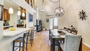 Une cuisine spacieuse avec un plancher en bois, un coin repas doté d’une longue table et de chaises, et un éclairage suspendu.
