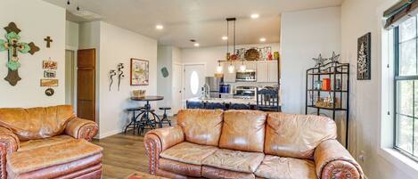 A spacious living room with a leather sofa and ottoman, a dining area, and a kitchen in the background.
