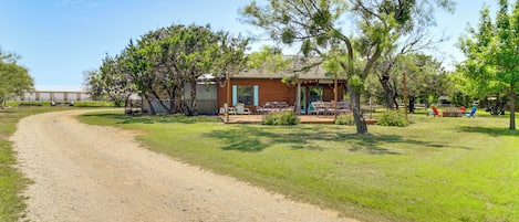 A rustic cabin with a dirt path leading to it, surrounded by trees and a clear sky.