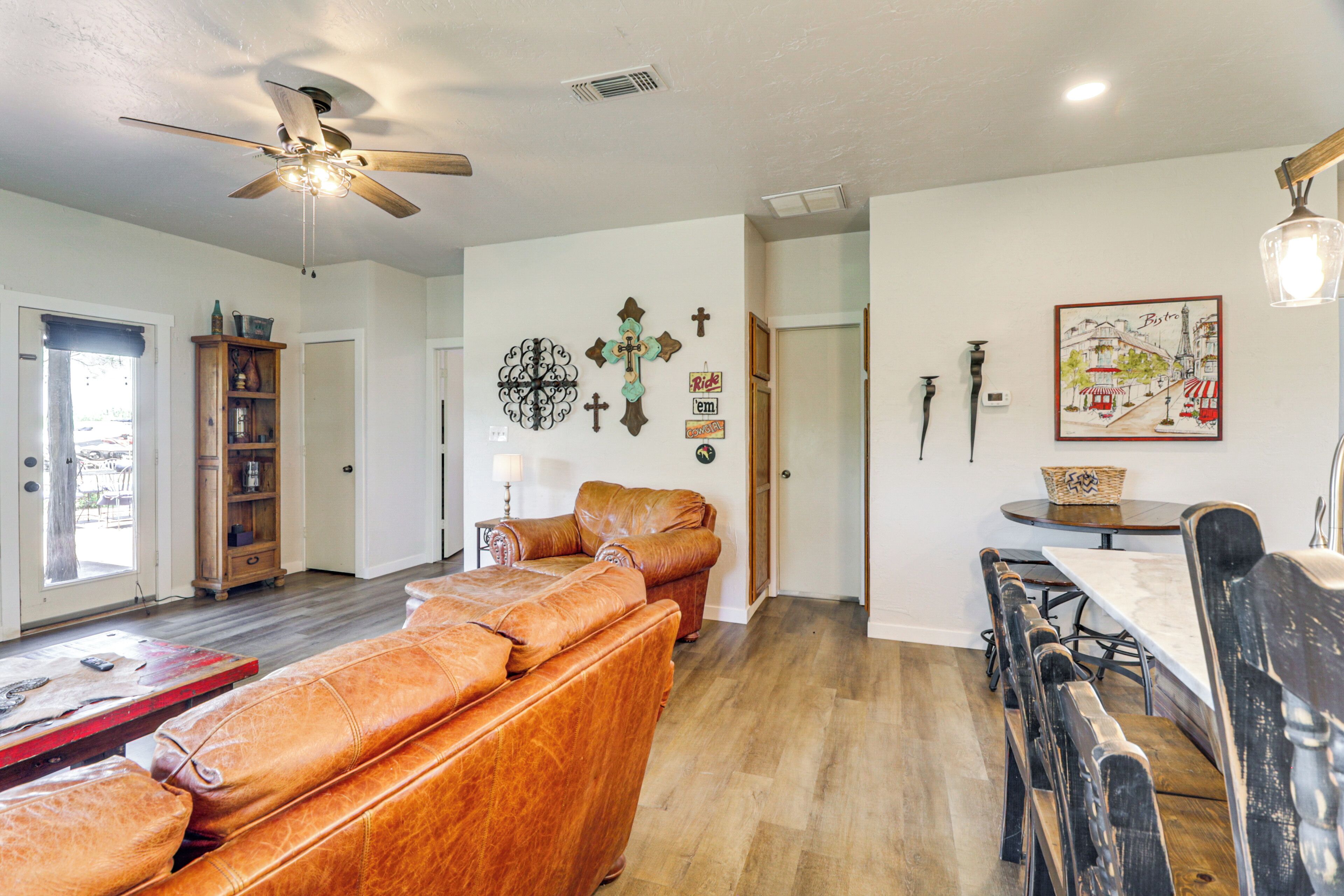 A spacious living room with a leather sofa, a dining table, and a ceiling fan.