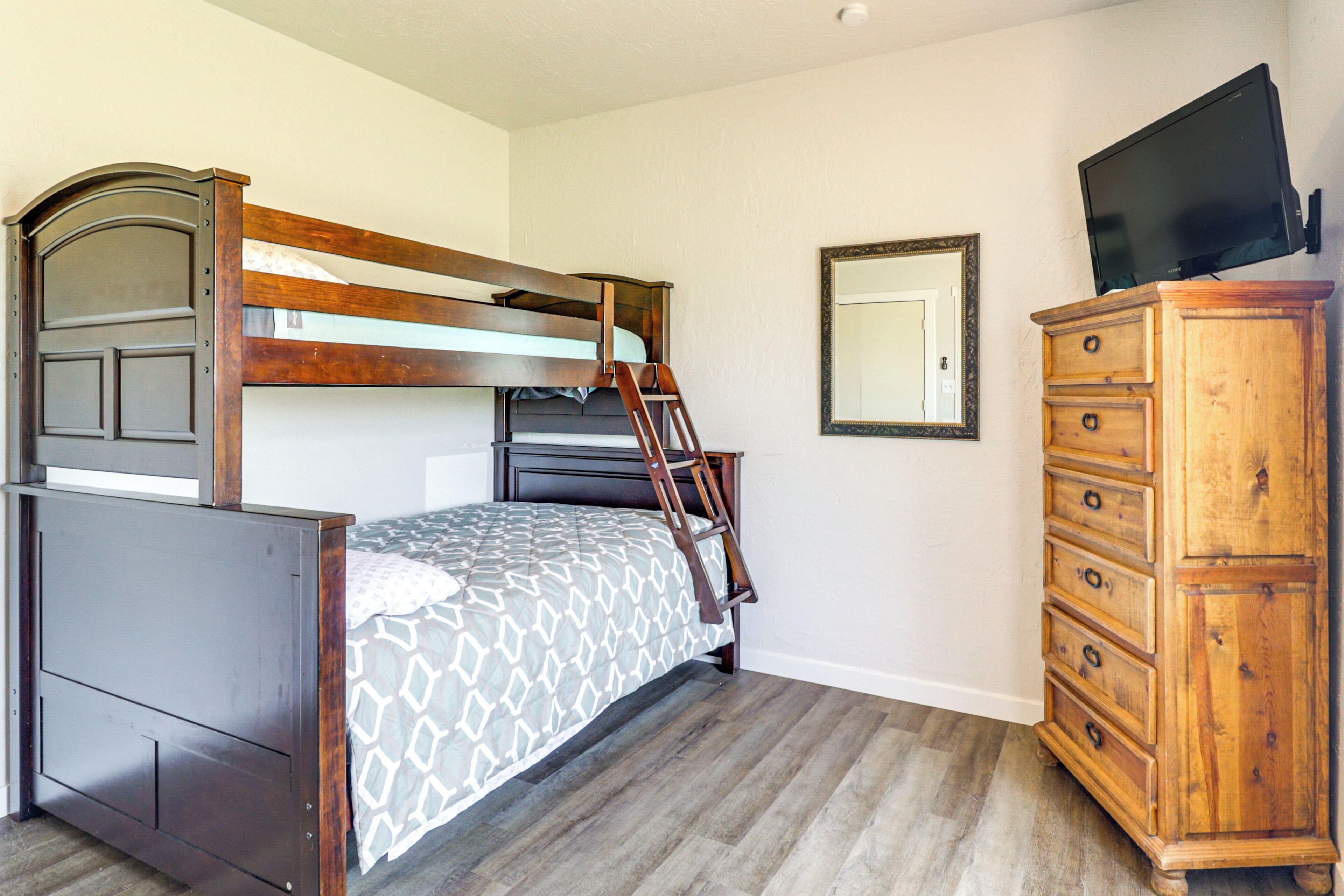 A bedroom with a bunk bed, a dresser, a mirror, and a television.