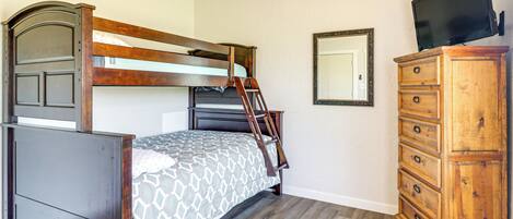 A bedroom with a bunk bed, a dresser, a mirror, and a television.