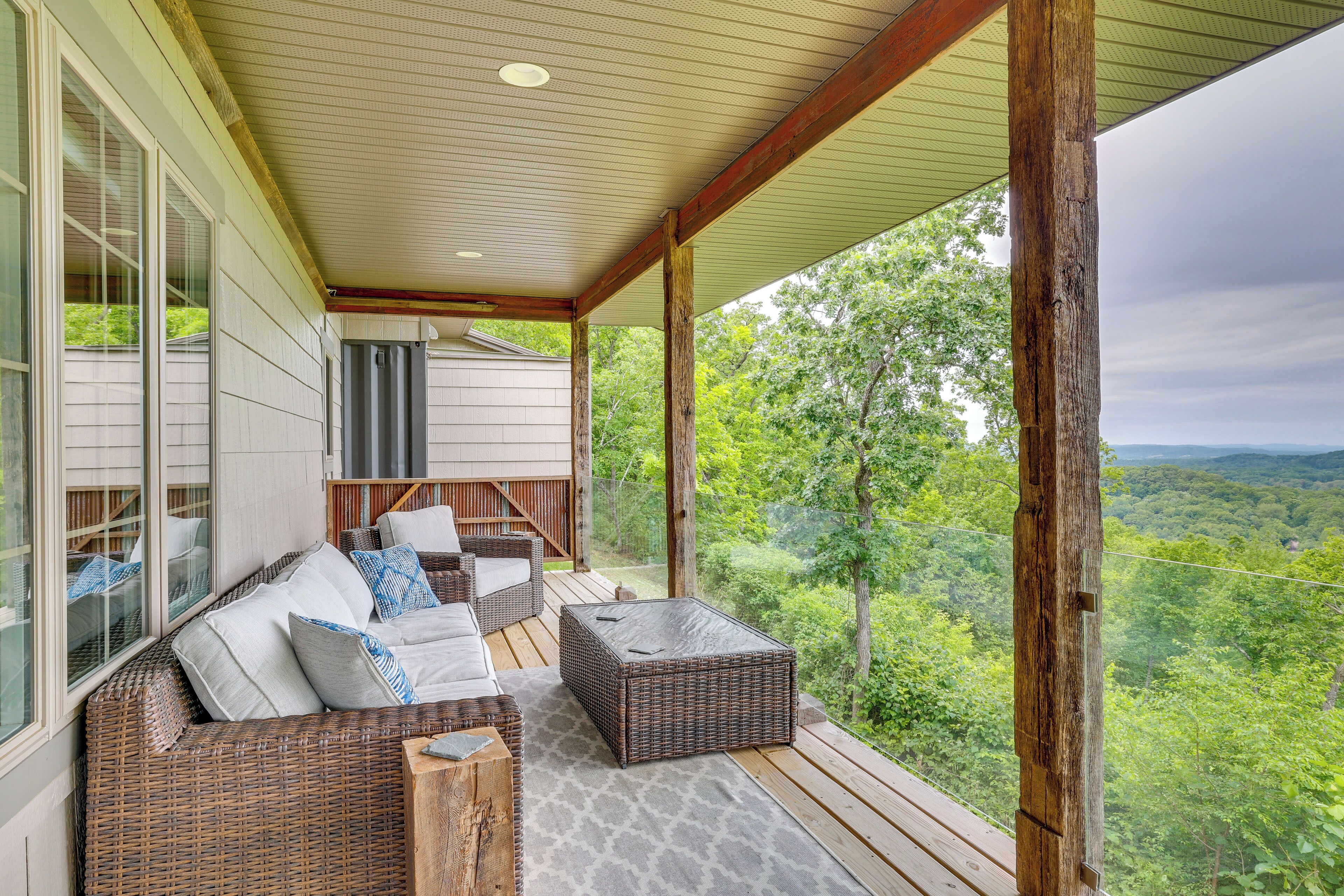 A covered porch with wicker furniture, a stone floor, and a view of a forested landscape.