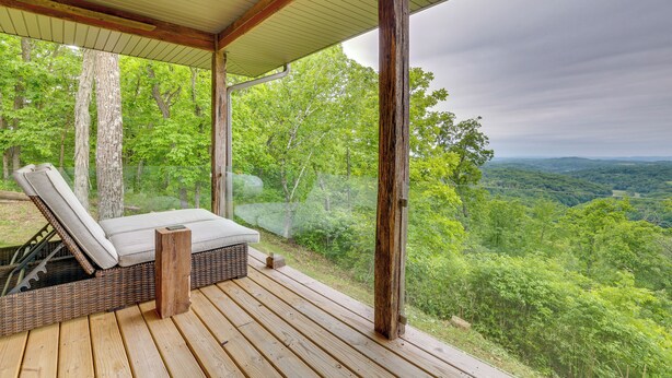 A wooden deck with a wicker lounge chair and a small table, overlooking a forested landscape. - Ski, Ice Fish & Snowshoe: Mindoro Getaway! (Mindoro)