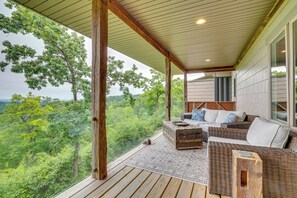 A covered outdoor seating area with wicker furniture and a view of a forested landscape.