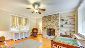 A living room with a stone fireplace, a ceiling fan, a leather sofa, a wooden coffee table, and a bookshelf. - Golf Course On-site: Spacious Hollidaysburg Home! (Hollidaysburg)