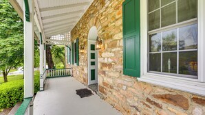 A stone building with a covered porch, green shutters, and a window with a view of the outdoors. - Golf Course On-site: Spacious Hollidaysburg Home! (Hollidaysburg)