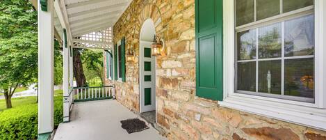 A stone building with a covered porch, green shutters, and a window with a view of the outdoors.
