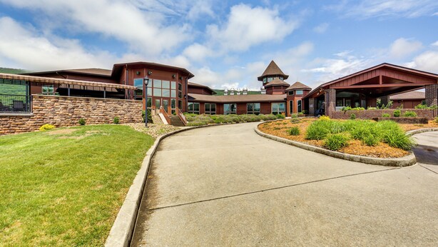 A modern building with a curved driveway, stone walls, and a tower-like structure. - Golf Course On-site: Spacious Hollidaysburg Home! (Hollidaysburg)