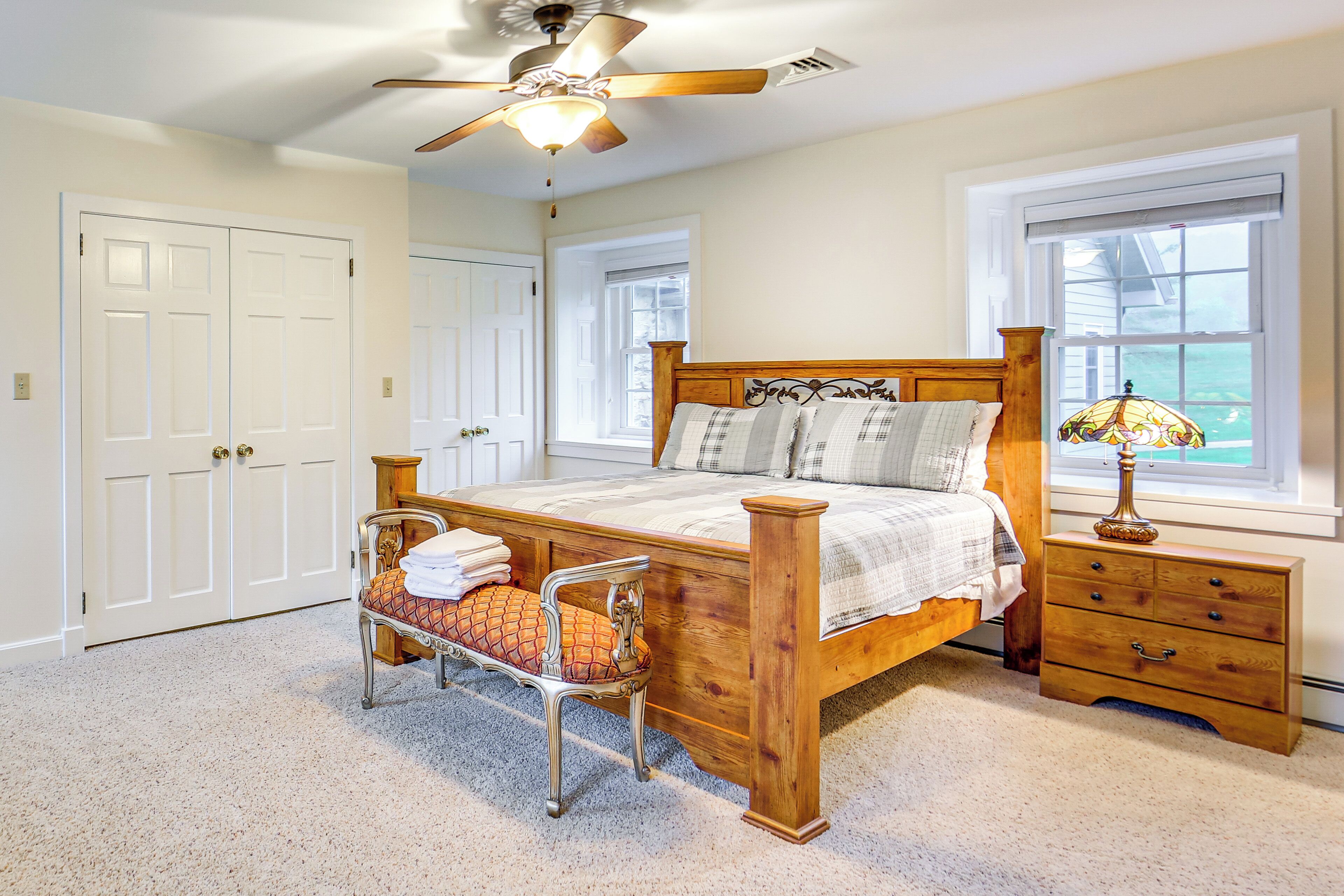 A bedroom with a wooden bed, a nightstand, a chair, a ceiling fan, and a window with a view.