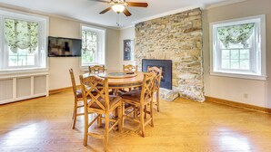 A dining room with a stone fireplace, wooden dining table, and chairs. - Golf Course On-site: Spacious Hollidaysburg Home! (Hollidaysburg)