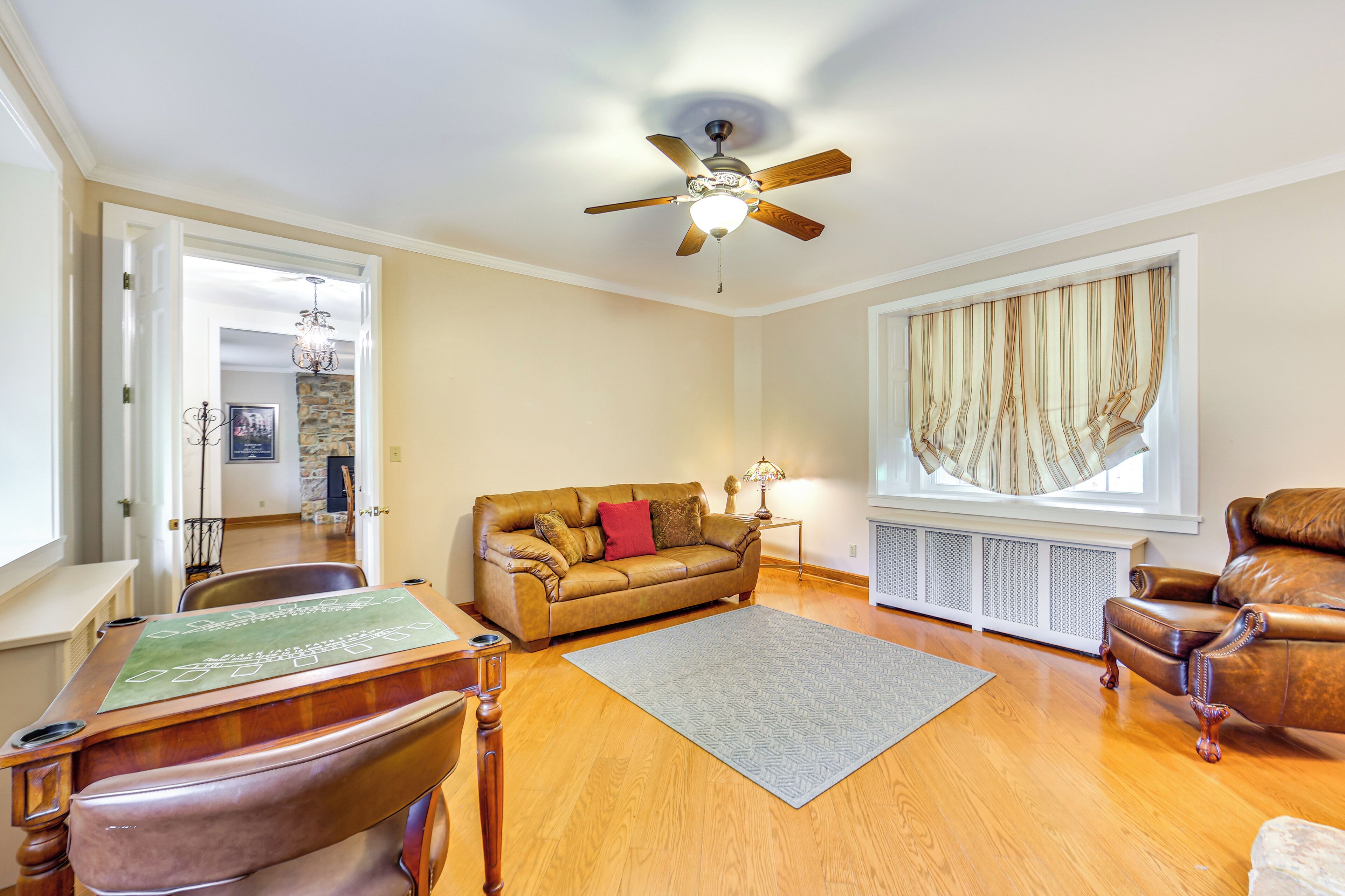 A living room with a brown leather sofa, a wooden coffee table, a ceiling fan, and a large window with curtains.