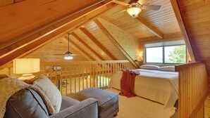 A cozy attic bedroom with a sloped ceiling, wooden beams, a bed, a couch, and a ceiling fan. - Bluff Views: 'bunker Hill' Cabin in Mindoro! (Mindoro)