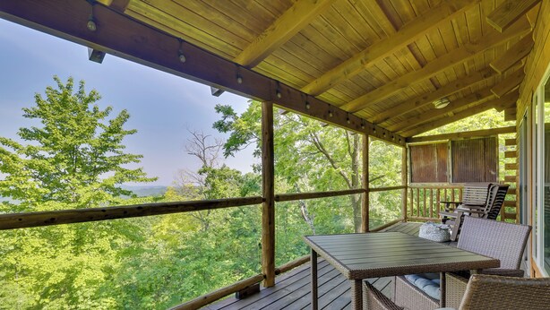 A covered outdoor deck with a table and chairs, surrounded by wooden railings, overlooking a forested area. - Bluff Views: 'bunker Hill' Cabin in Mindoro! (Mindoro)