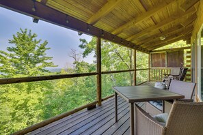 Una terraza techada al aire libre con una mesa y sillas, rodeada de barandas de madera, con vistas a una zona boscosa.