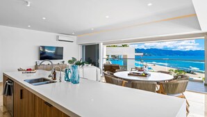 A modern kitchen with a large island, a dining area with wicker chairs, and a view of the ocean. - Beachfront, Private Pool, Theatre Room, Views! (Puerto Vallarta)