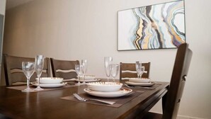 Uma mesa de jantar posta com pratos, tigelas e copos de vinho, com um quadro abstrato moderno na parede.