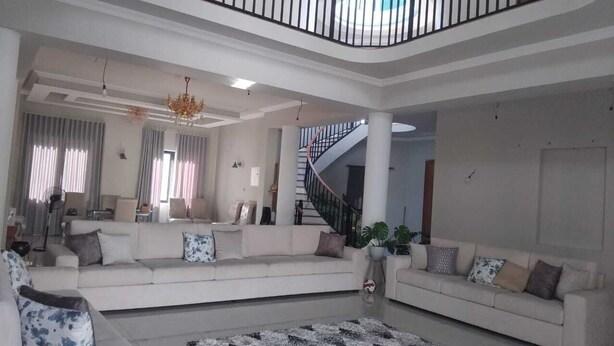 Amplia sala de estar con un amplio sofá, una araña y una escalera que lleva a un piso superior.