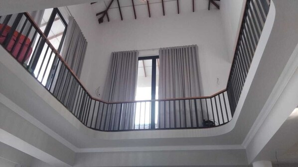 Ein modernes Interieur mit einer geschwungenen Treppe, einem großen Fenster mit Vorhängen und einer Decke mit sichtbaren Holzbalken.