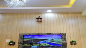 Un téléviseur à écran plat fixé sur un mur en bois agrémenté d’un panneau décoratif en bois, une petite étagère avec une plante et un luminaire décoratif placé au-dessus du téléviseur.