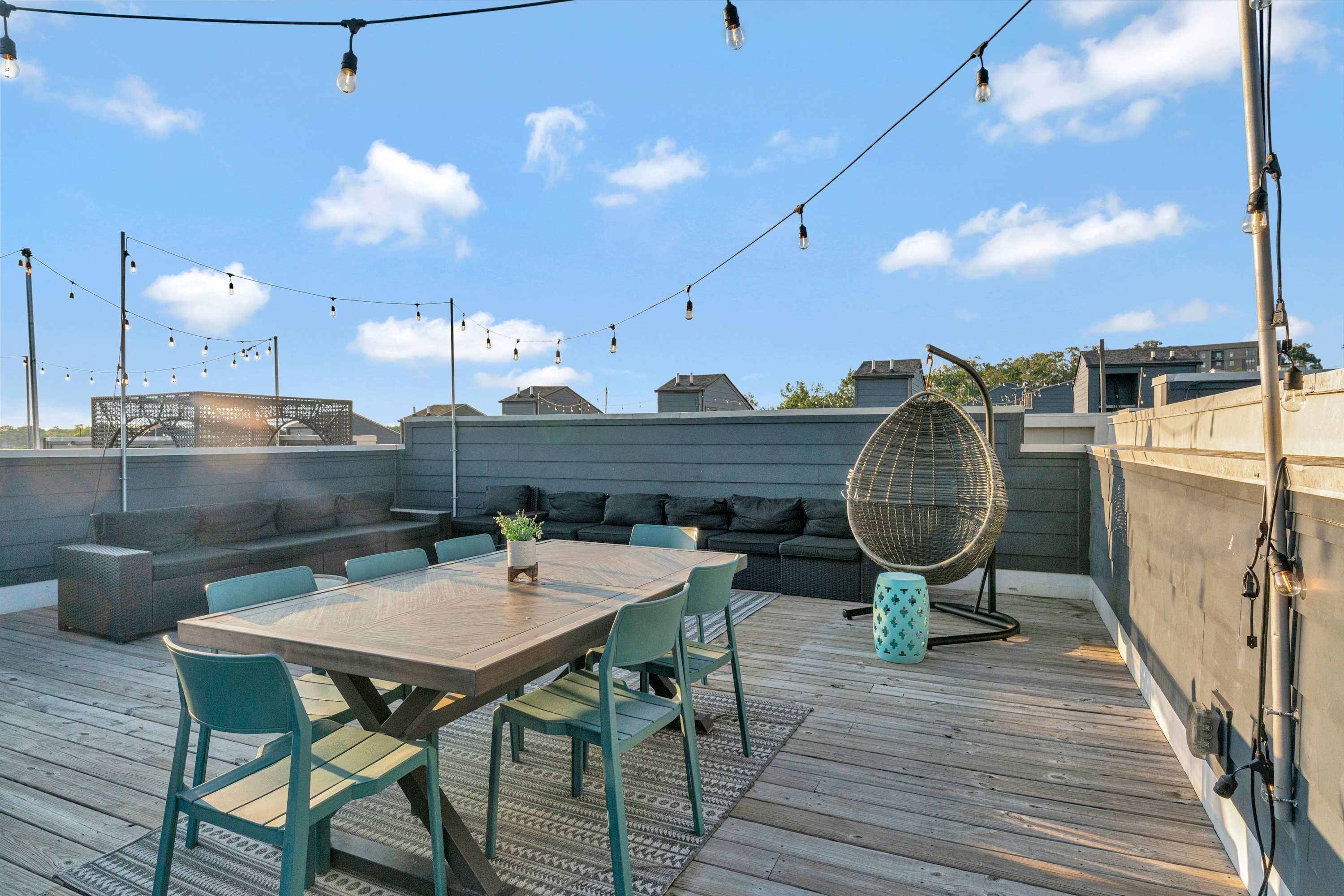 An outdoor deck with a wooden table and chairs, a wicker fan, and a seating area with cushions.