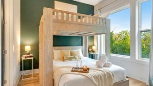 A bedroom with a bunk bed, bedside tables, a bedside lamp, a tray with bottles and a candle, and a view of greenery outside. - Rooftop Deck 2 Car Garage Near Downtown Nashville (Nashville)