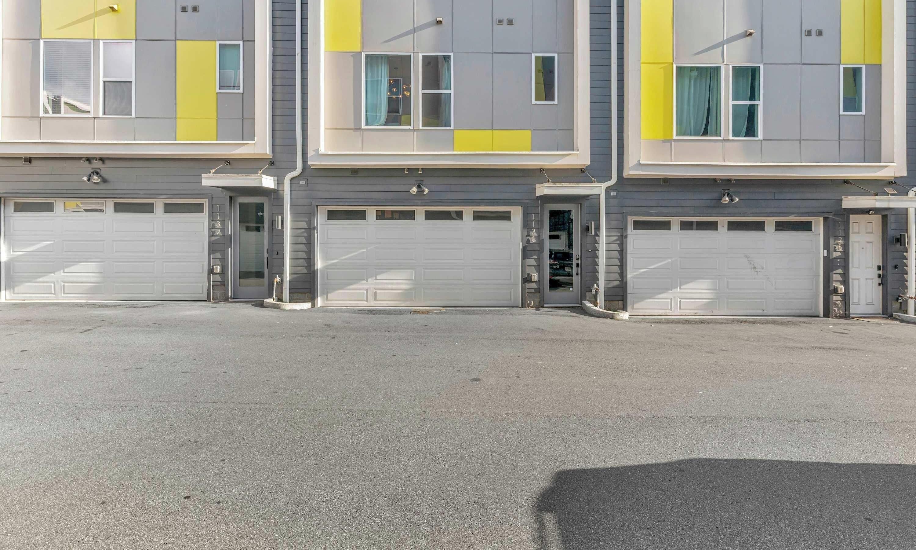 A row of three garage doors with a grey and yellow facade, each with a white garage door.