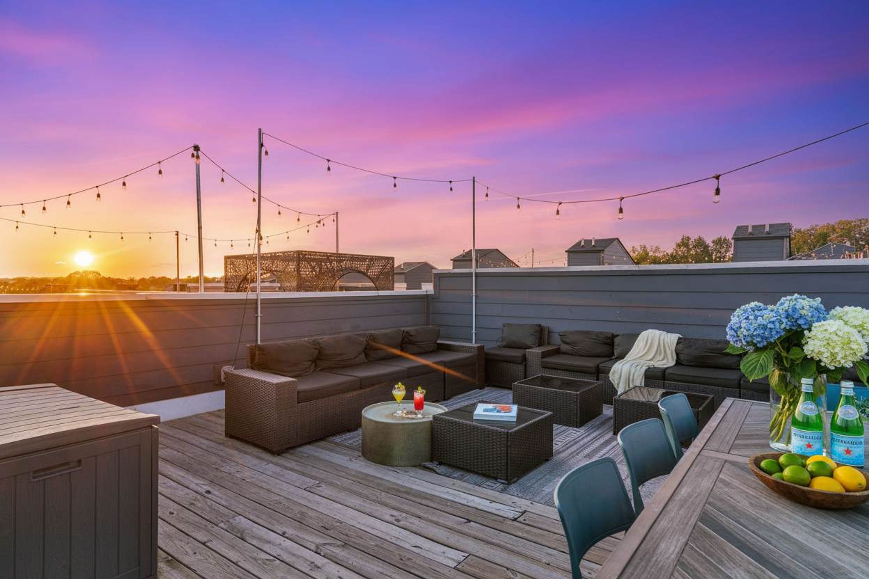 A rooftop patio with outdoor seating, string lights, and a sunset view.