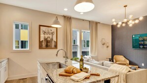 A modern kitchen with a granite countertop, a built-in oven, and a sink. There is a large window with curtains, a chandelier, and a framed picture on the wall. - Rooftop Deck 2 Car Garage Near Downtown Nashville (Nashville)