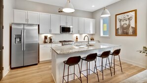 A modern kitchen with white cabinets, stainless steel appliances, and a central island with bar stools. - Rooftop Deck 2 Car Garage Near Downtown Nashville (Nashville)