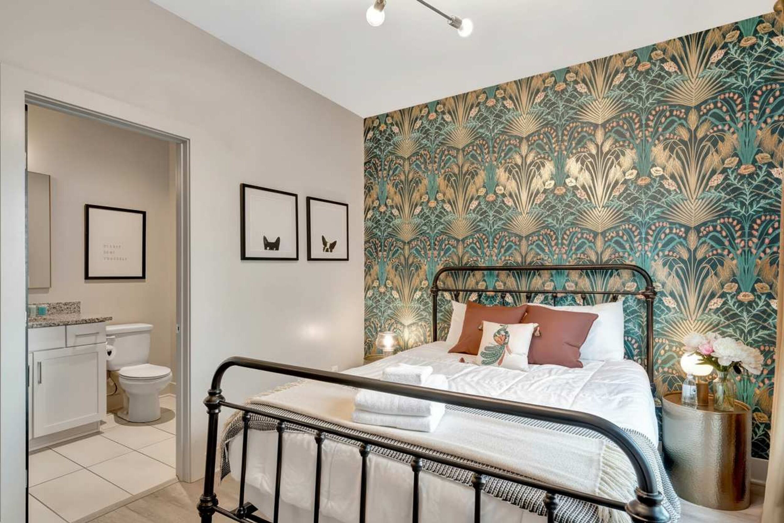 Une chambre avec un lit, une salle de bain avec des toilettes et un mur orné d’un motif floral.